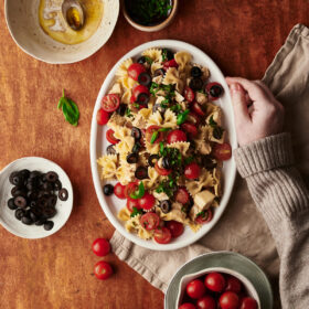 caprese pasta salad recipe plate with the ingredients on a table and one hand