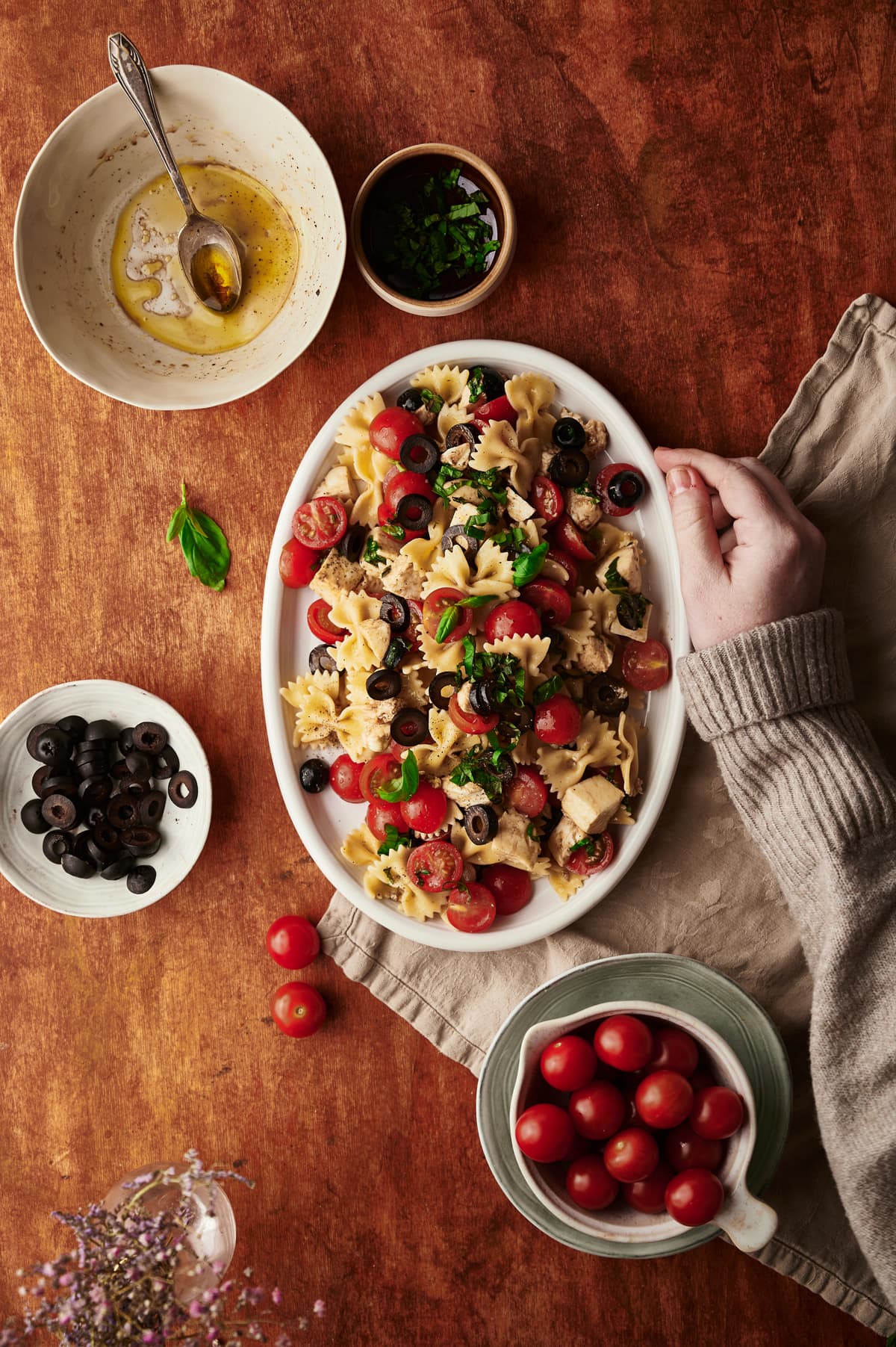 caprese pasta salad recipe plate with the ingredients on a table and one hand