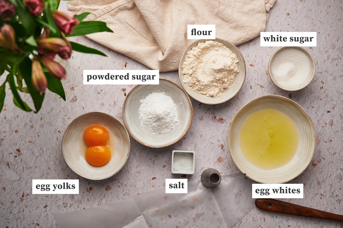 picture of ingredients for lady fingers recipe on a table: sugar, flour, egg whites, egg yolks, powdered sugar and salt.