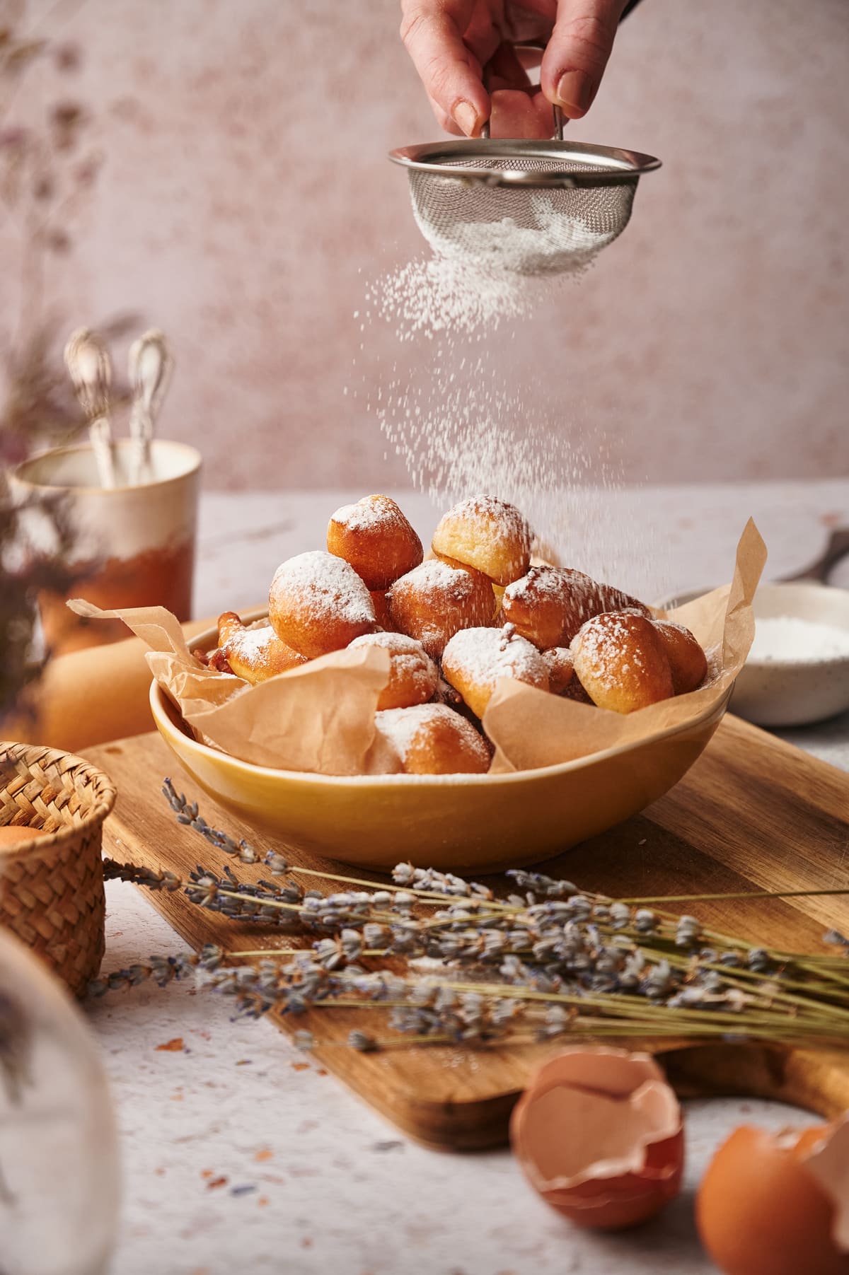 picture of zeppole on a serving bowl with an hand dusting them with powdered sugar