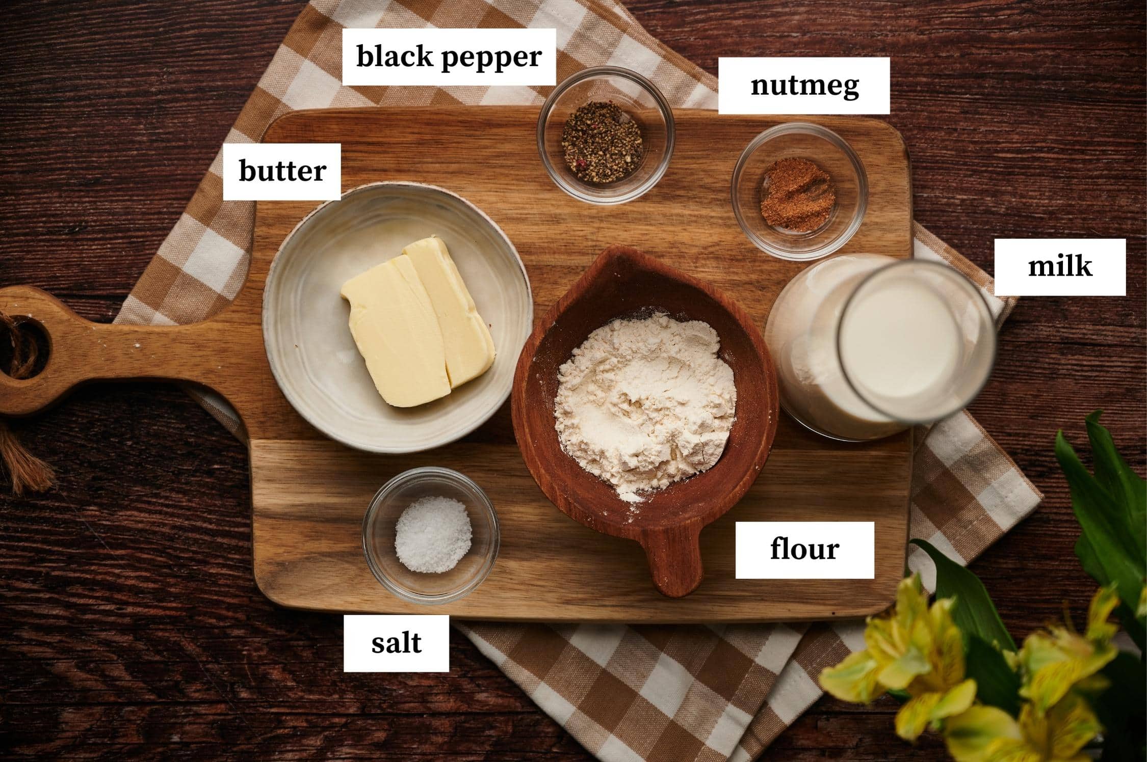 besciamella ingredients white sauce layed on a table: butter, black pepper, nutmeg, milk, flour and salt.