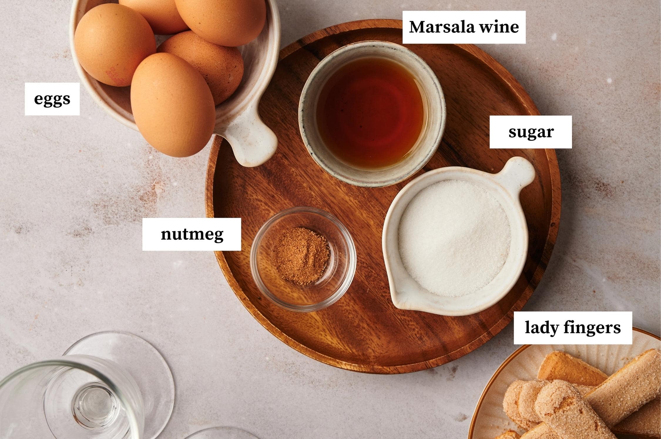 ingredients for zabaglione recipe on a table: eggs, nutmeg, sugar, lady fingers, marsala wine