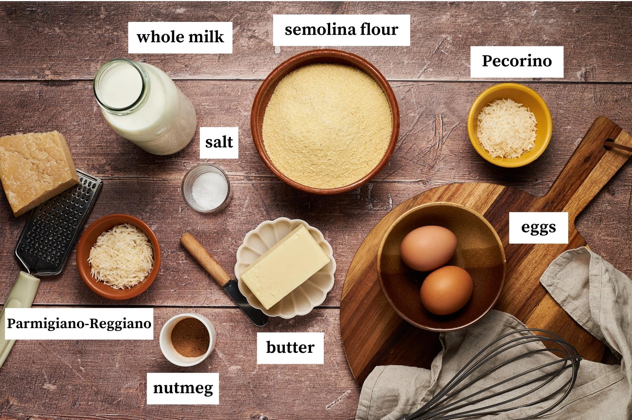 ingredients for gnocchi alla romana displayed on a table: whole milk, semolina flour, pecorino cheese, parmigiano reggiano cheese, eggs, nutmeg, butter.