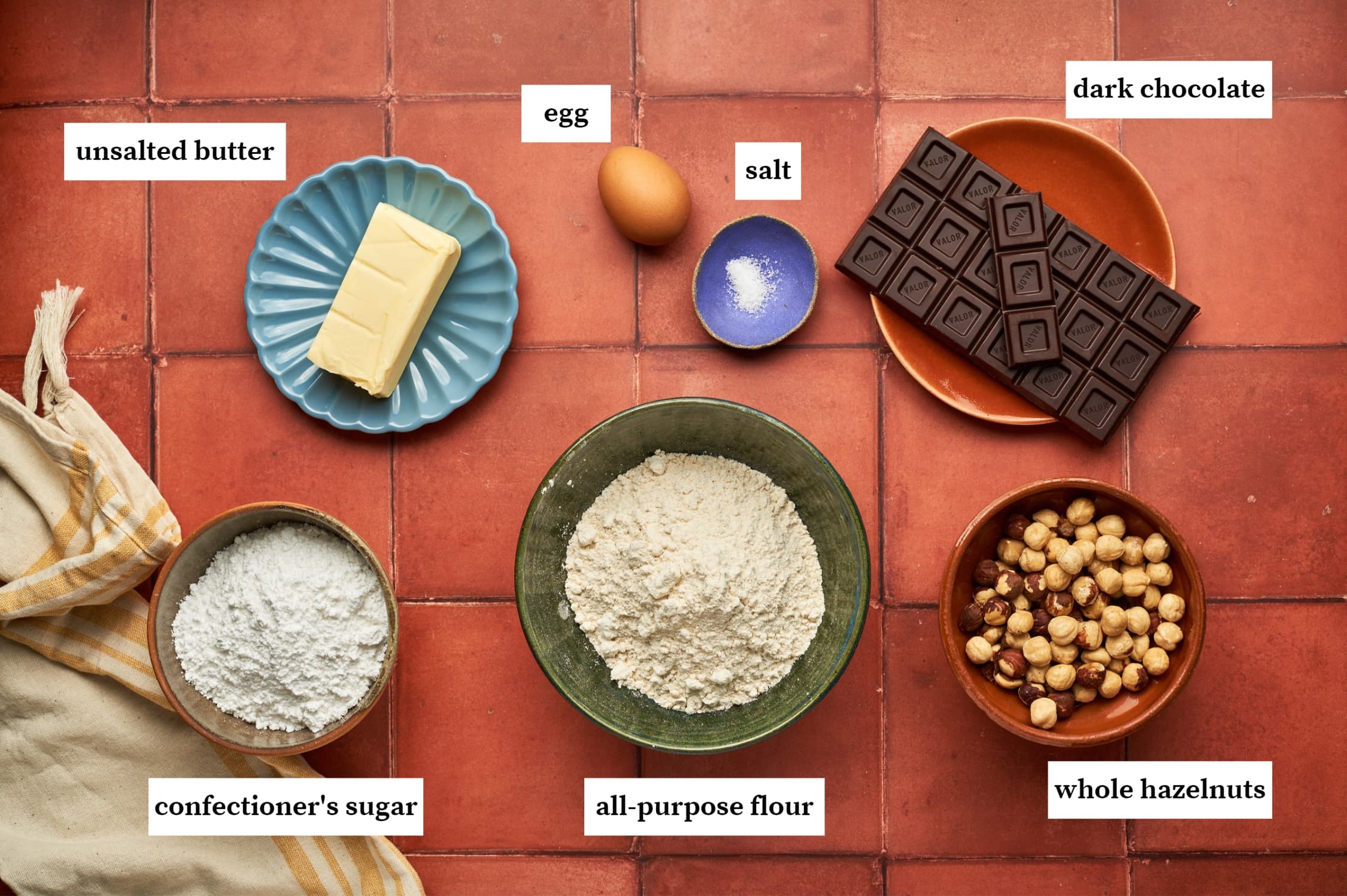 ingredients for baci di dama italian cookies including unsalted butter, egg, salt, dark chocolate, confectioner's sugar all-purpose flour and whole hazelnuts.