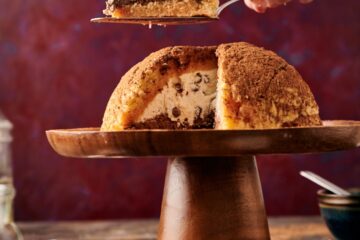 wooden cake stand with a zuccotto. a hand holding a cake cutter and a slice of zuccotto