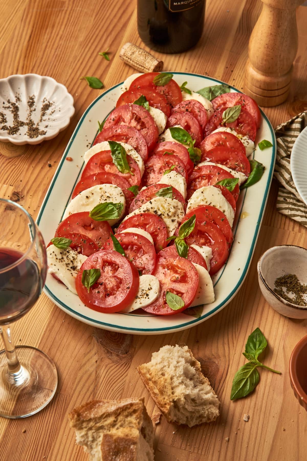 oval plate with caprese salad. next to a glass of wine, bread, bottle of wine.