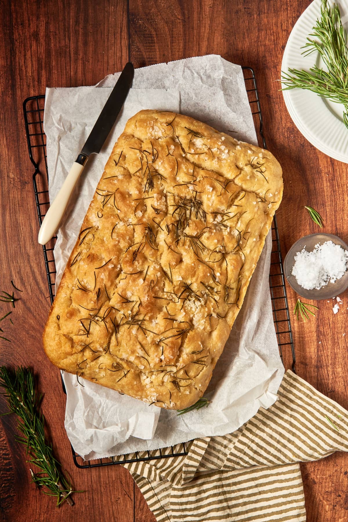 focaccia bread on top of a cooling rack with parchment paper with a bread knife.
