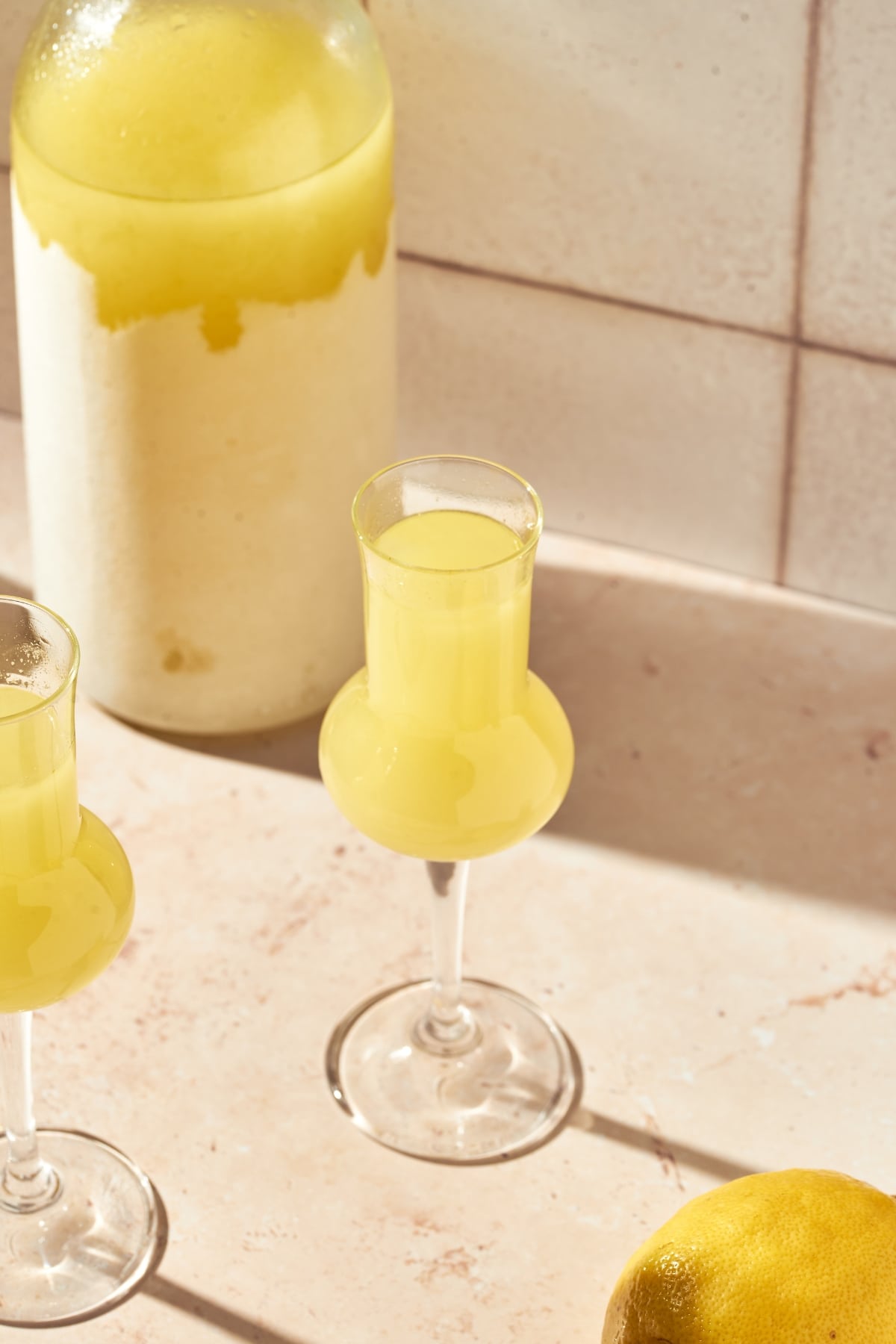 Two glasses of homemade limoncello next to a lemon.