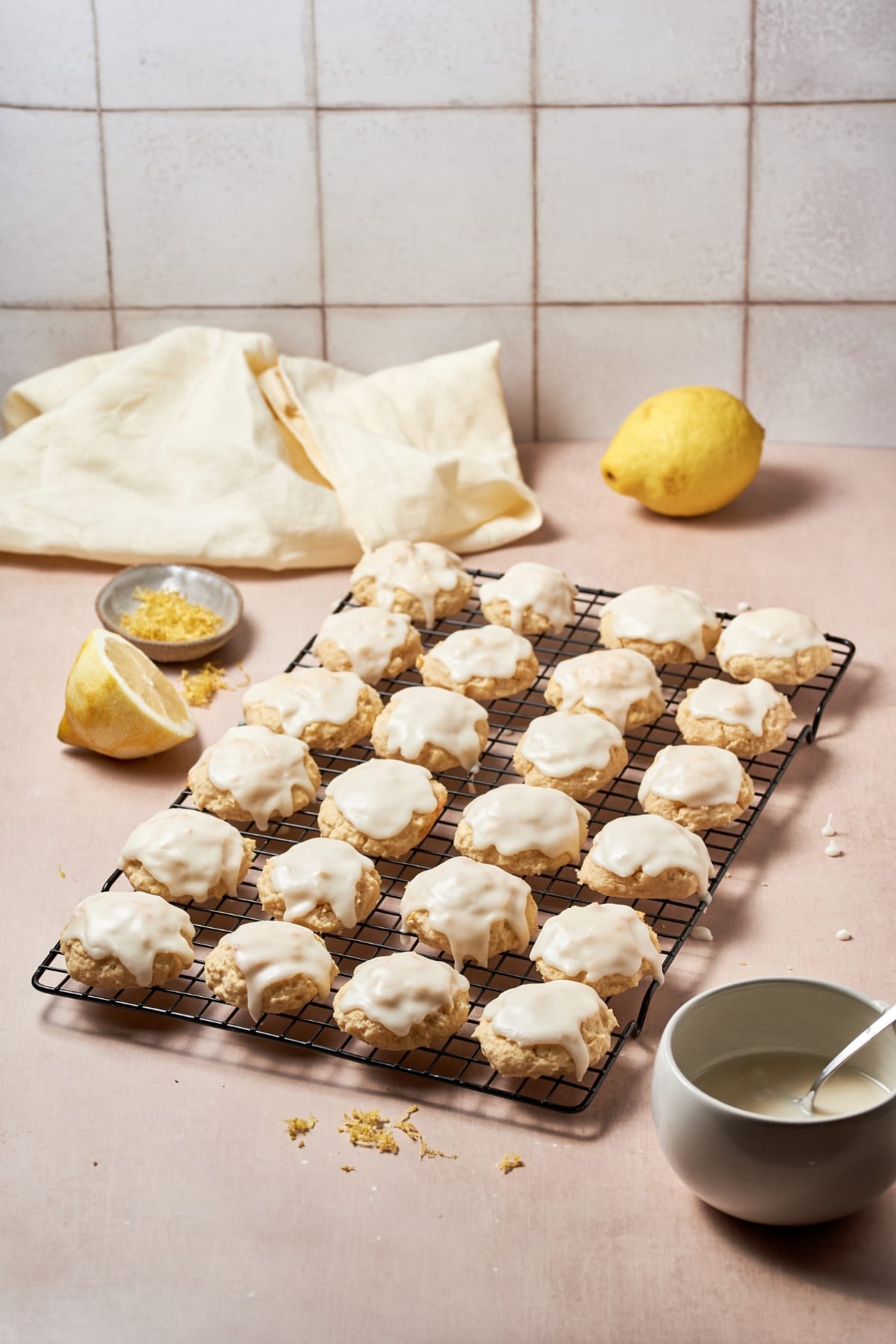 Frosted ricotta cookies on a baking wire next to half of lemon.