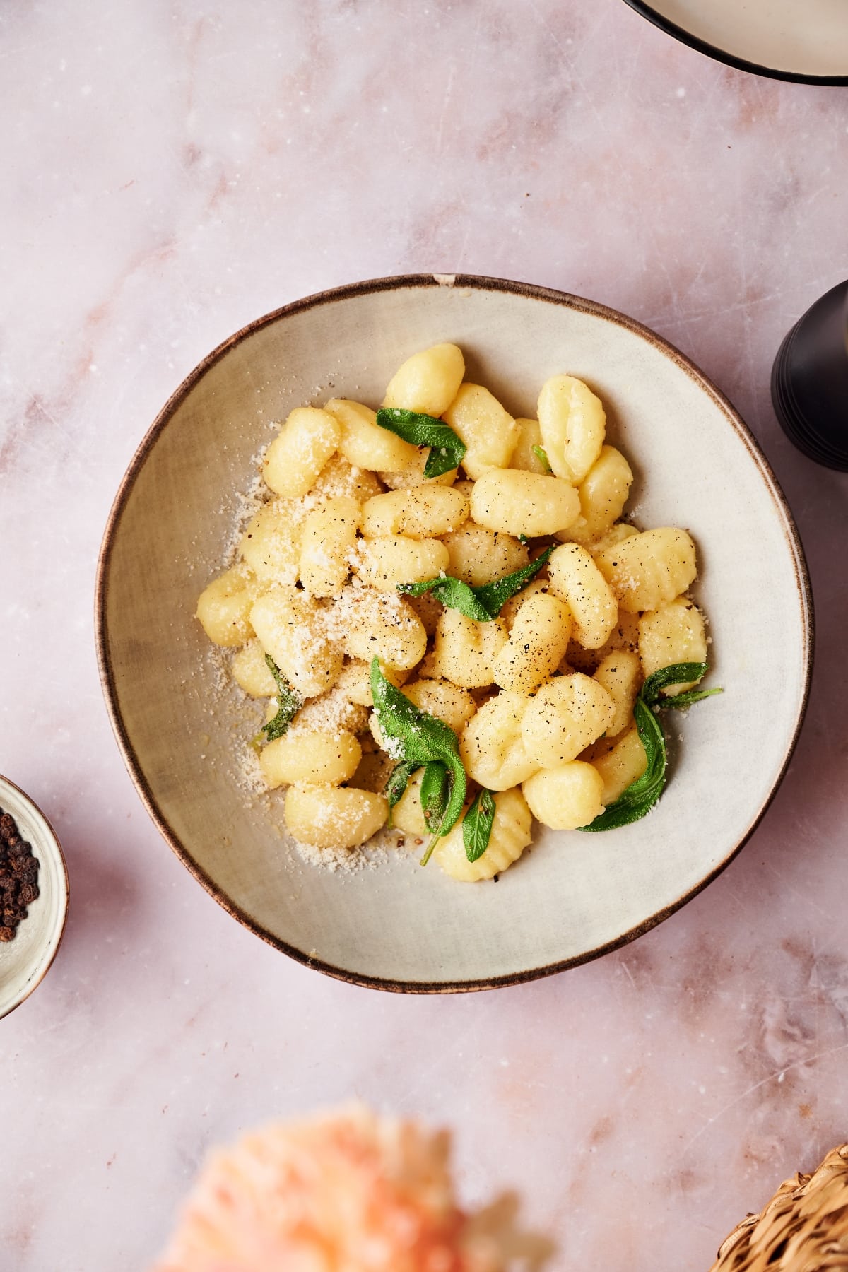 finished plate of potato gnocchi on a brown plate topped with sage, ground black pepper and parmesan cheese