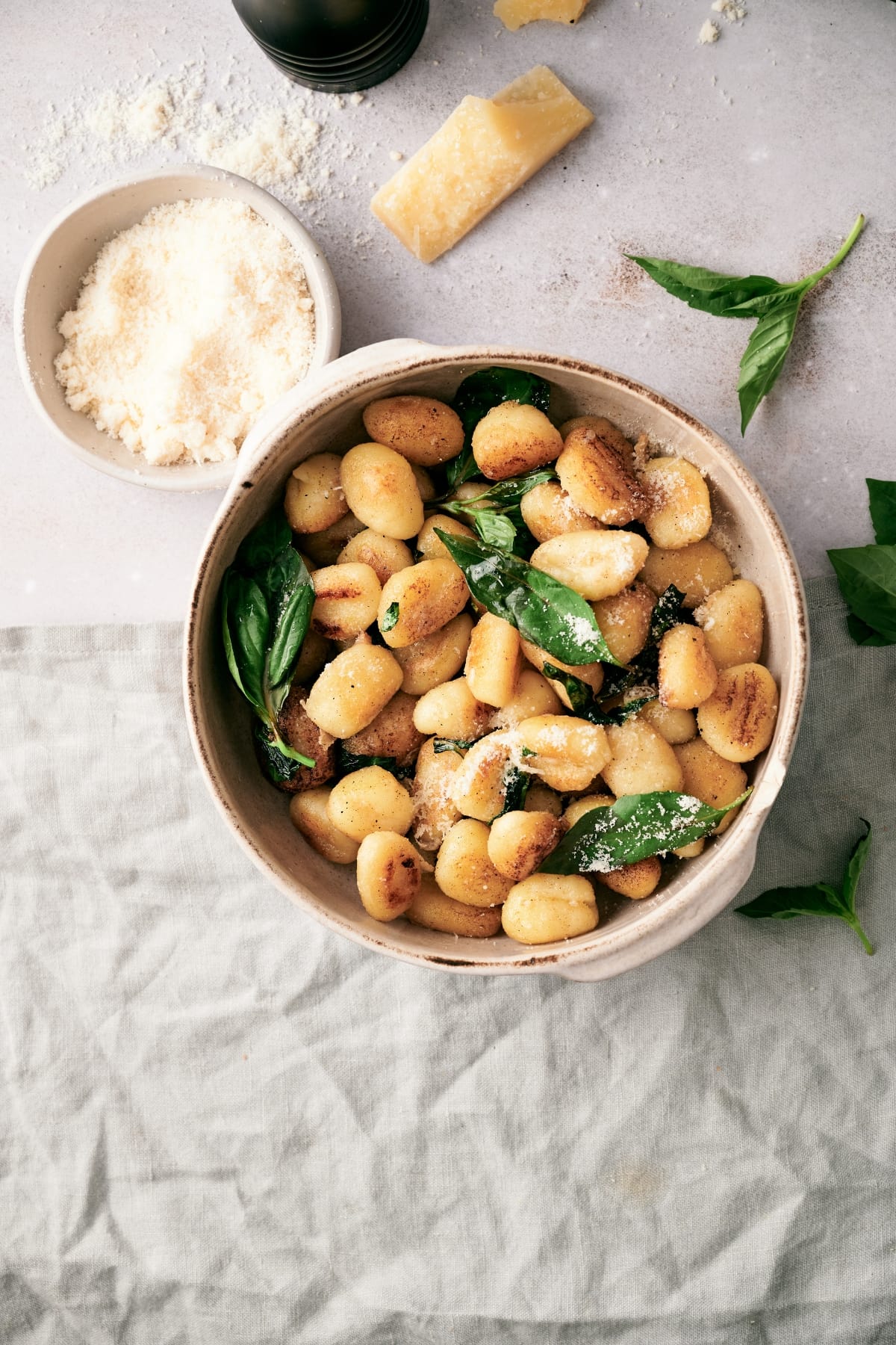 pan-fried gnocchi in a bowl beside a bowl of grated romano cheese
